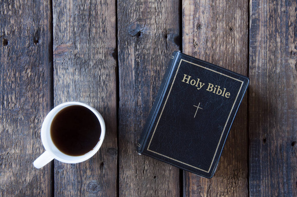 Black bible on a wooden table. White cup with tea or coffee. View from above - Foto, immagini