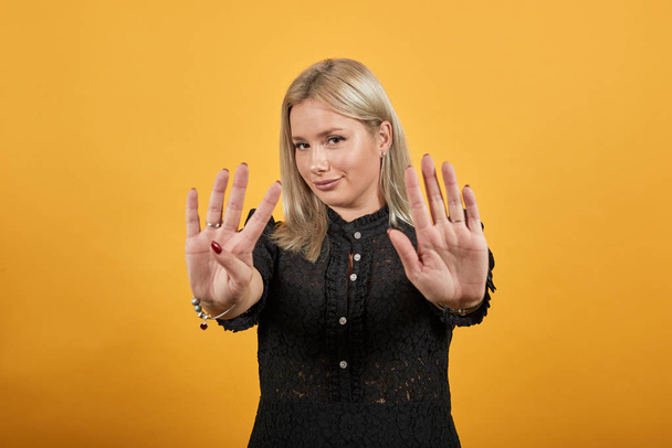 girl in black dress on yellow background happy woman shows nine fingers smiles - Фото, изображение