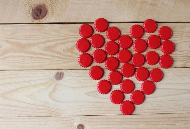 A red love heart made from beer bottle tops viewed top down on a rustic wooden table. Beer drinkers Valentine's day concept - Photo, Image
