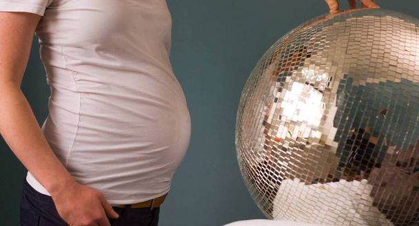 Pregnant woman in a white shirt standing in front of a disco ball - Zdjęcie, obraz