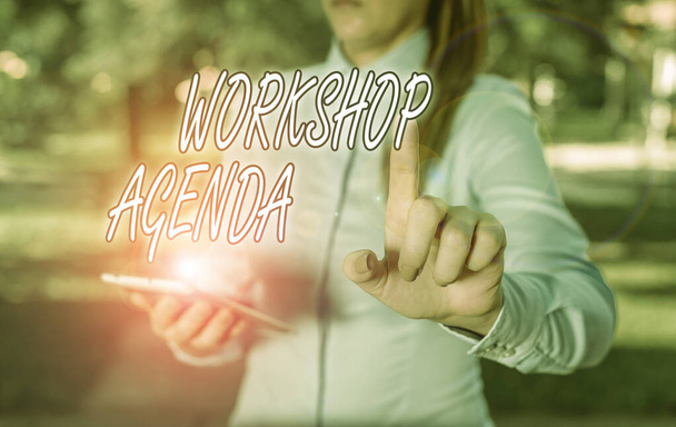 Text sign showing Workshop Agenda. Business photo text helps you to ensure that your workshop stays on schedule Woman in a blue business shirts pointing with her finger into empty space - Photo, Image