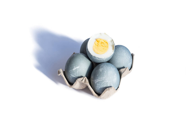 Karton tepside beton renginde dört Paskalya yumurtası ve bir haşlanmış yumurta beyaz arka planda kesilir. Mutlu Paskalyalar. Boşluğu kopyala. - Fotoğraf, Görsel
