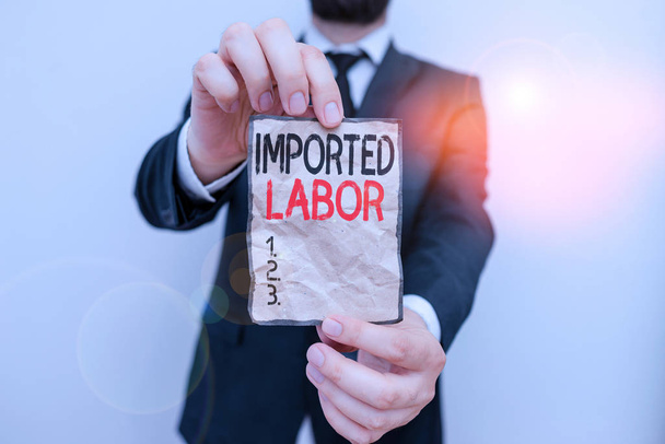 Text sign showing Imported Labor. Business photo showcasing human who works in a country which he or she is not a citizen Male human wear formal work suit office look hold notepaper sheet use hand - Photo, Image