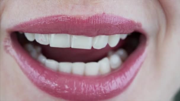 Στενή άποψη του γυναικείου στόματος και της γλώσσας γλείφει τα χείλη με σέξι ροζ κραγιόν και δείχνει τέλεια λευκά δόντια - Πλάνα, βίντεο