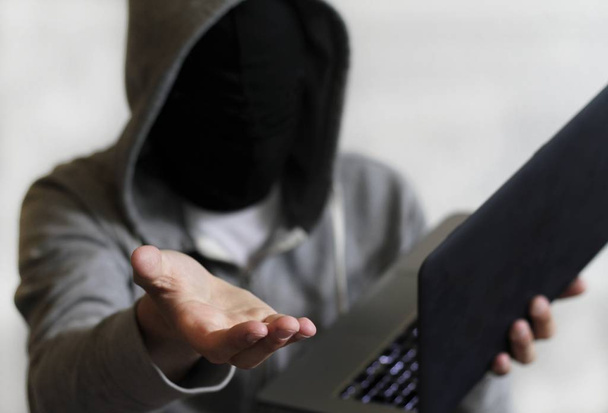 A mysterious male holding a laptop with his hand towards the camera - Photo, image