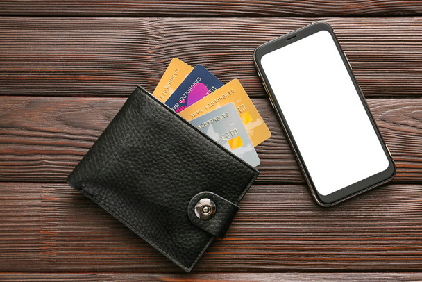 Karty kredytowe z portfelem i komórką na drewnianym tle. Pojęcie bankowości internetowej - Zdjęcie, obraz