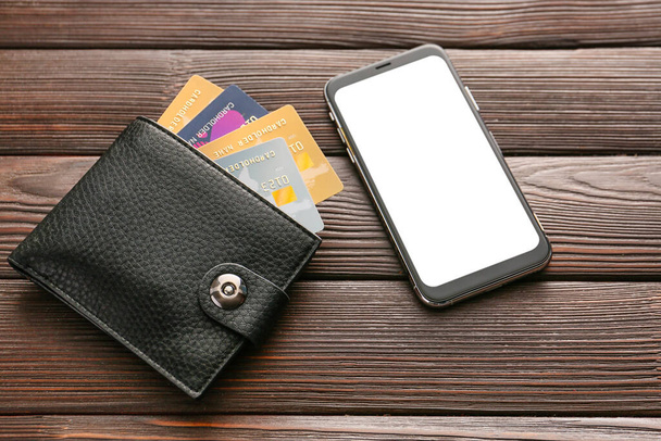 Kredietkaarten met portemonnee en mobiele telefoon op houten achtergrond. Concept van online bankieren - Foto, afbeelding