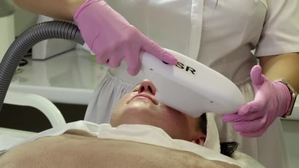 Eine Frau bereitet sich im Salon auf eine Laser-Verjüngung vor. Ein Kosmetologe und Dermatologe vervollständigt die Photorejuvenation. Schießen aus verschiedenen Blickwinkeln - Filmmaterial, Video
