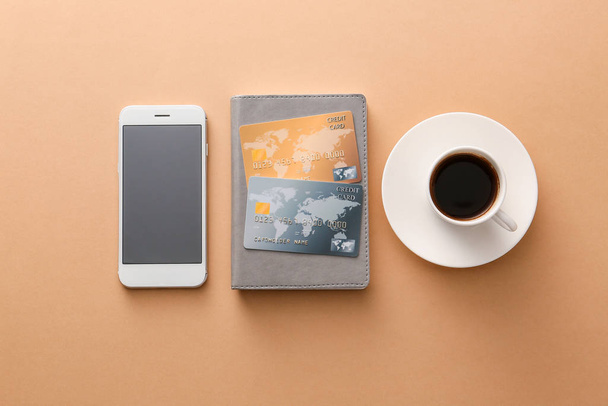 Tarjetas de crédito con teléfono móvil y taza de café sobre fondo de color. Concepto de banca en línea
 - Foto, imagen