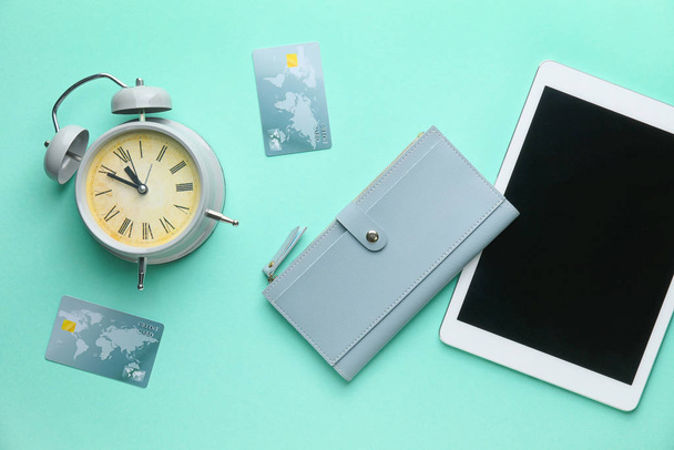 Wallet with tablet computer, credit cards and alarm clock on color background - Photo, image