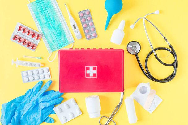 First aid kit red box with medical equipment and medications for emergency top view on pastel yellow background. - Φωτογραφία, εικόνα