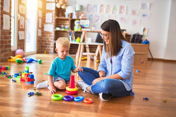 Young caucasian child playing at playschool with teacher. Mother and son at playroom with intelligence toy - Photo, Image