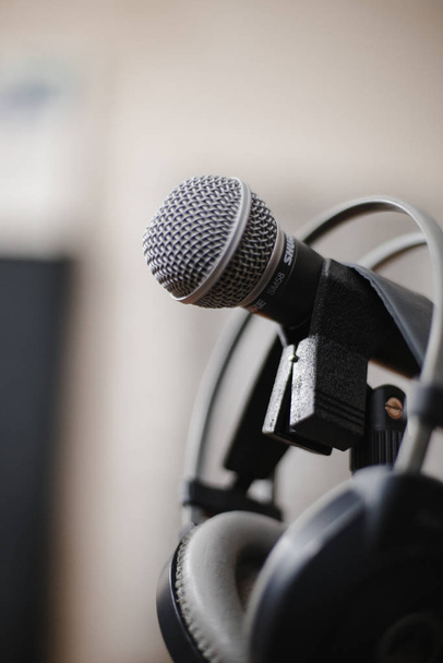 grijszwarte over-ear hoofdtelefoon hangt aan een studiomicrofoon en microfoonstandaard voor geluidsopname. Een nieuw nummer opnemen in een muziekstudio. Goede geluids- en geluidskwaliteit. Kopieerruimte.  - Foto, afbeelding