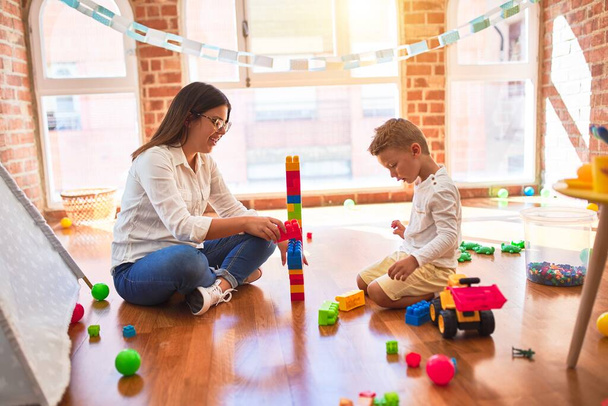 Belle enseignante et tout-petit jouant avec des blocs de construction autour de beaucoup de jouets à la maternelle
 - Photo, image