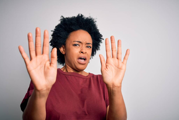 Jonge mooie Afro-Amerikaanse afro vrouw met krullend haar draagt casual t-shirt staan bang en doodsbang met angst uitdrukking stoppen gebaar met de handen, schreeuwen in shock. Paniekconcept. - Foto, afbeelding