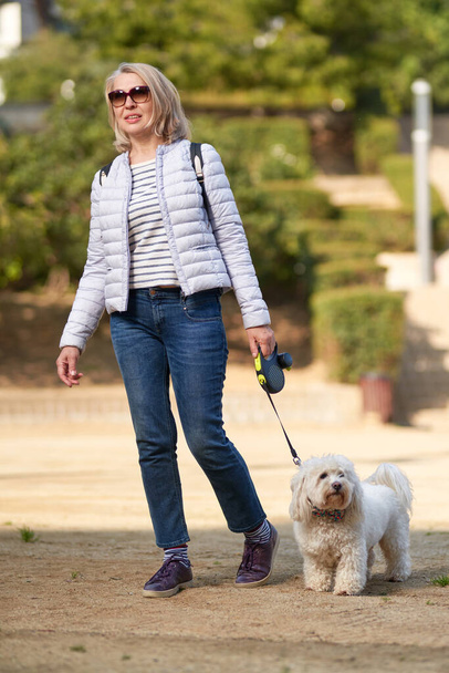 attractive middle-aged blond woman walking with dog in summer city - Foto, afbeelding