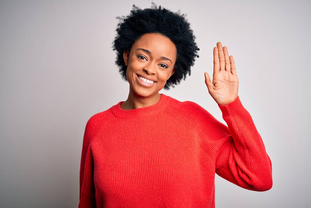 Jeune belle afro afro-américaine aux cheveux bouclés portant un pull décontracté rouge Renonçant à dire bonjour heureux et souriant, geste de bienvenue amical
 - Photo, image