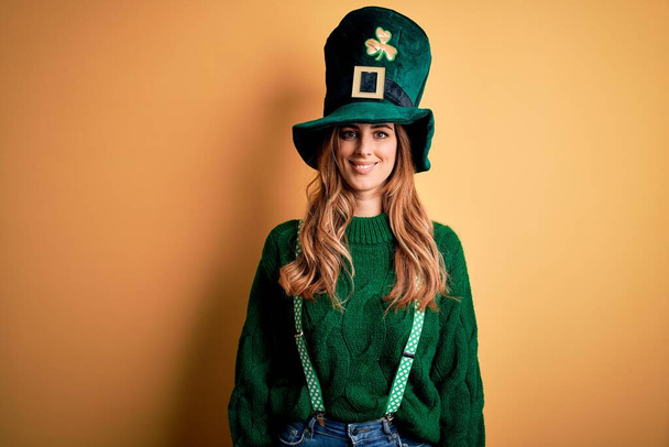 Mulher morena bonita usando chapéu verde com trevo celebrando dia santo patricks com um sorriso feliz e legal no rosto. Pessoa com sorte
. - Foto, Imagem