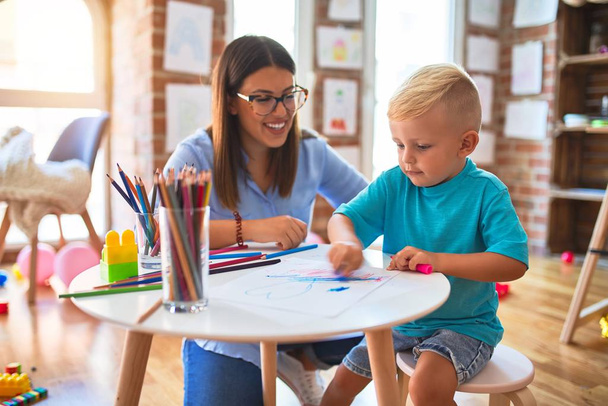 Νεαρό καυκάσιο παιδί που παίζει στο σχολείο με δάσκαλο. Μητέρα και γιος στο playroom ζωγραφίζουν με χρωματιστά μολύβια - Φωτογραφία, εικόνα