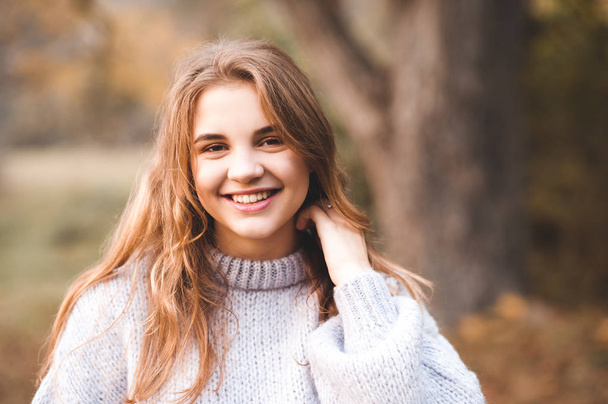 Glimlachend tienermeisje van 16-17 jaar in gebreide trui poserend in park close-up. Portret van een gelukkige tiener. Ik kijk naar de camera. Twintiger jaren.  - Foto, afbeelding