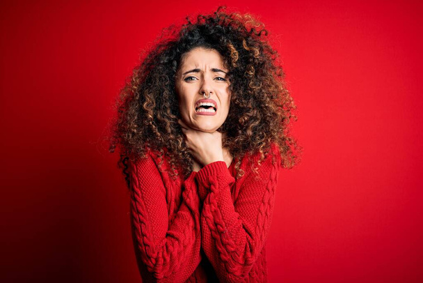 Young beautiful woman with curly hair and piercing wearing casual red sweater shouting suffocate because painful strangle. Health problem. Asphyxiate and suicide concept. - Foto, afbeelding