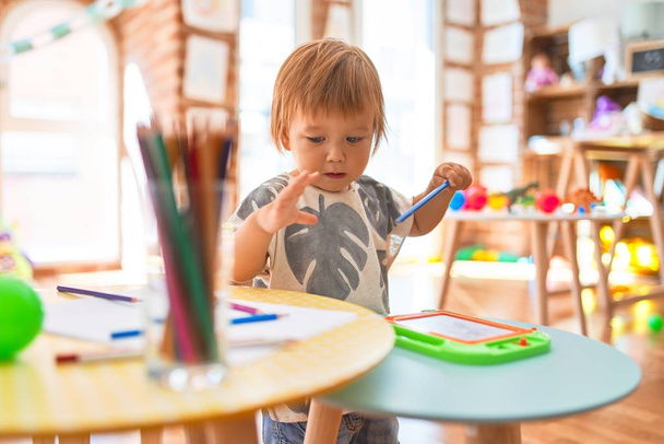 Dibujo adorable del niño pequeño usando tablero digital alrededor de porciones de juguetes en el jardín de infantes
 - Foto, Imagen