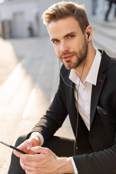 Hadsome young businessman wearing earphones standing - Foto, Imagen