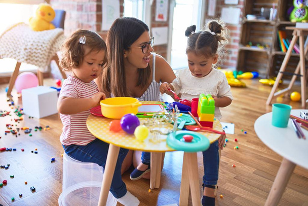 Jeune belle enseignante et tout-petits jouant des repas en utilisant de la nourriture en plastique et des couverts jouet à la maternelle
 - Photo, image