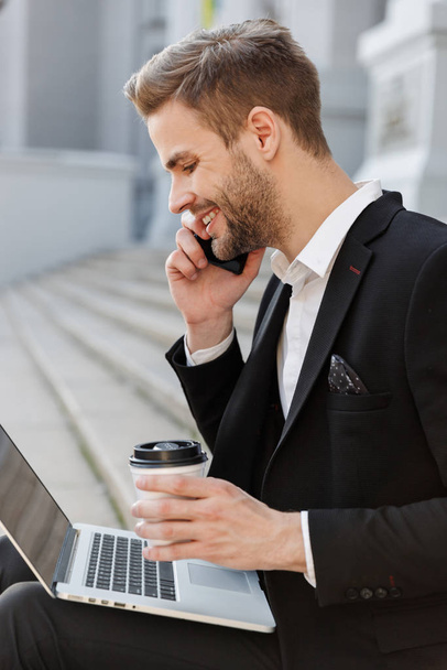 Attractive young businessman wearing suit using mobile phone - Foto, Bild