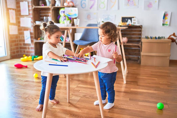 Anaokulundaki masada bir sürü renkli kalemle oynayan sevimli bebekler. - Fotoğraf, Görsel