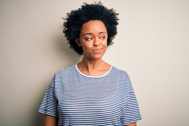 Fiatal gyönyörű afro-amerikai nő göndör haj visel csíkos póló mosolygós oldalra néz, és bámul félre gondolkodás. - Fotó, kép