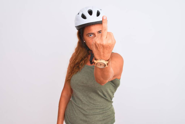 Dojrzała rowerzystka w średnim wieku, nosząca kask bezpieczeństwa na odizolowanym tle Pokazuje środkowy palec, niegrzeczny i niegrzeczny wyraz twarzy - Zdjęcie, obraz