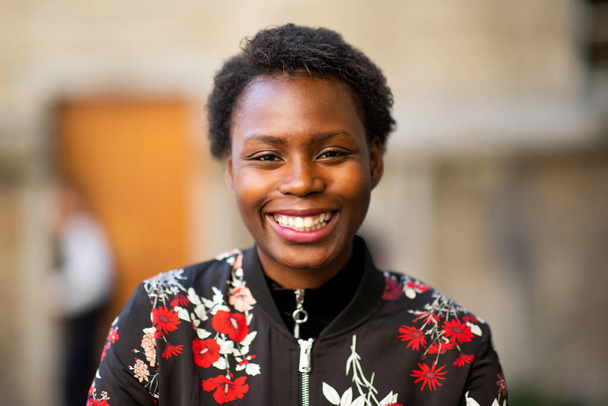 Закрыть портрет красивой молодой африканской женщины, улыбающейся размытым фоном
 - Фото, изображение