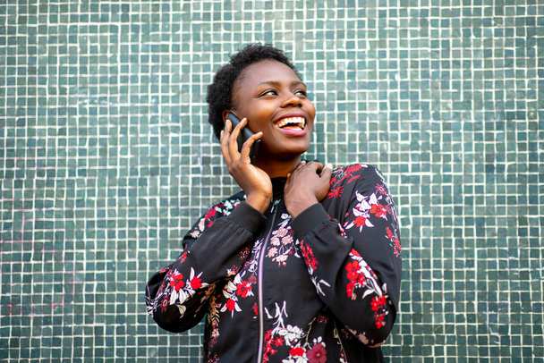 Закрыть портрет счастливая африканка, прислонившаяся к стене и разговаривающая с мобильником
 - Фото, изображение