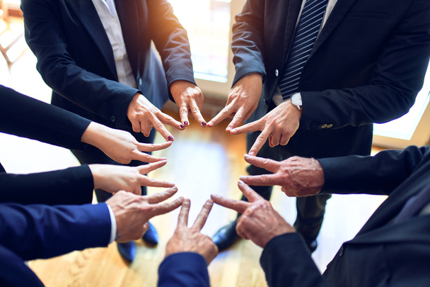 Üzletemberekből álló csoport, akik egy körön állnak és szimbólumot csinálnak ujjaikkal az irodában.. - Fotó, kép