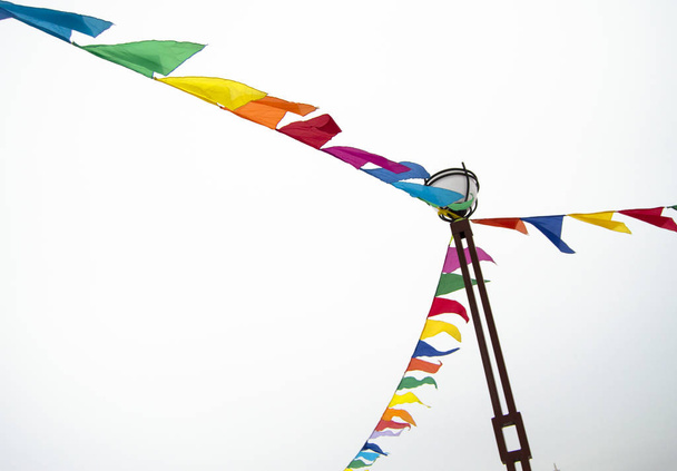 Праздничные треугольные флаги в виде гирлянд прикреплены к фонарному столбу. Декоративные идеи в праздновании события, изолированные на белом фоне
 - Фото, изображение