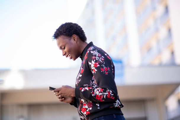Side portrait happy young african woman looking at mobile phone and laughing - 写真・画像