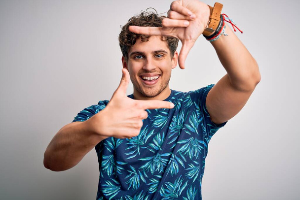 Young blond handsome man on vacation with curly hair wearing casual summer t-shirt smiling making frame with hands and fingers with happy face. Creativity and photography concept. - Photo, Image