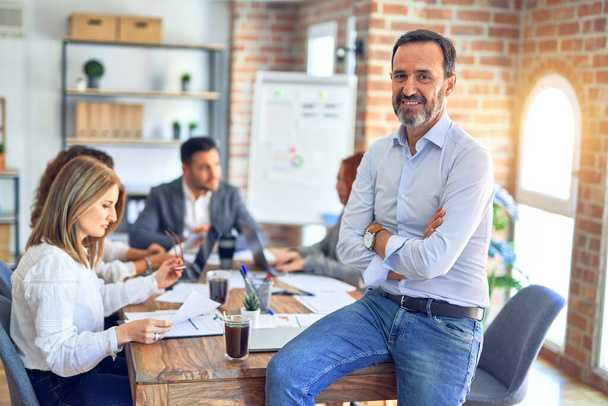 Group of business workers working together. Middle age handsome businessman standing smiling happy looking at the camera at the office - Photo, Image