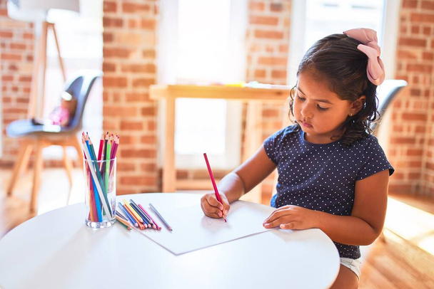 Όμορφο κοριτσάκι ζωγραφίζει χαριτωμένο σχέδιο χρησιμοποιώντας χρωματιστά μολύβια στο νηπιαγωγείο - Φωτογραφία, εικόνα