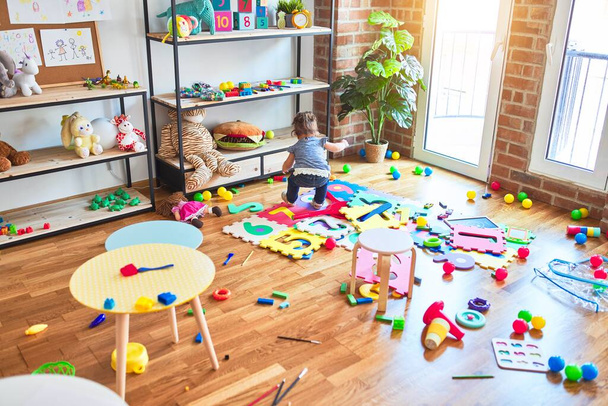 Piękny maluch siedzi na podłodze bawiąc się klockami zabawkami w przedszkolu - Zdjęcie, obraz