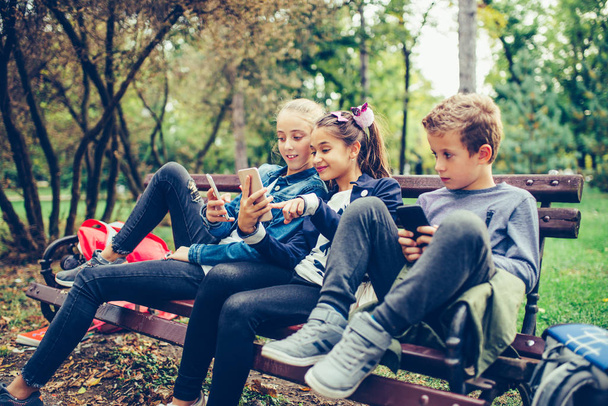 Gruppo di amici che utilizzano lo smartphone mentre sono seduti sulla panchina in
 - Foto, immagini