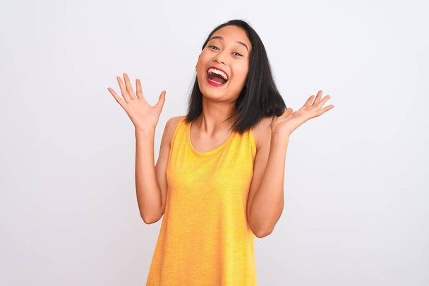 Mujer china joven con camiseta casual amarilla de pie sobre un fondo blanco aislado celebrando loco y sorprendido por el éxito con los brazos levantados y los ojos abiertos gritando emocionados. Concepto ganador
 - Foto, imagen