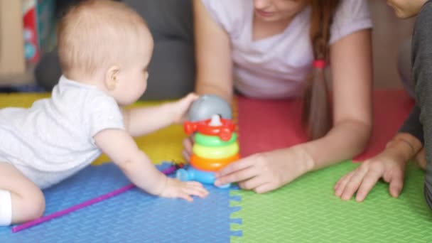 Woman, man and their baby are playing on the floor on a colorful rug and parents are teaching son to assemble a toy pyramid. Family and teaching children concept. Front view medium shot in 4K video. - Video