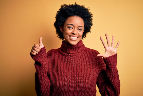 junge schöne afrikanisch-amerikanische Afrofrau mit lockigem Haar trägt lässigen Rollkragenpullover und zeigt mit Finger Nummer sechs nach oben, während sie selbstbewusst und glücklich lächelt. - Foto, Bild