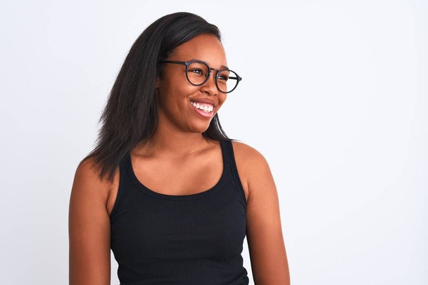 Belle jeune femme afro-américaine portant des lunettes sur fond isolé regardant de côté avec le sourire sur le visage, expression naturelle. Rire confiant
. - Photo, image