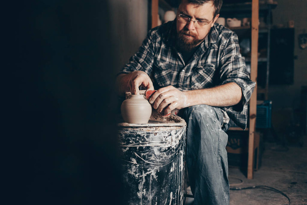 Adam çömlekçi çarkında çalışıyor ve bir sürahi kil yaratıyor. - Fotoğraf, Görsel