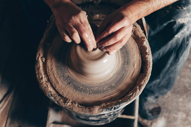 Homem forma um produto de argila branca em uma visão superior da roda de cerâmica
 - Foto, Imagem