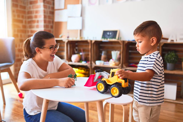 Beautiful teacher and toddler boy playing with tractor and cars at kindergarten - Photo, Image