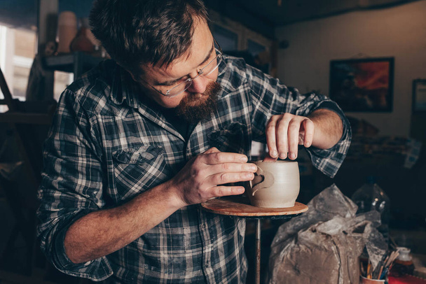 Бородатий чоловік працює в керамічній майстерні, зосереджуючись на процесі створення глиняної чашки
 - Фото, зображення
